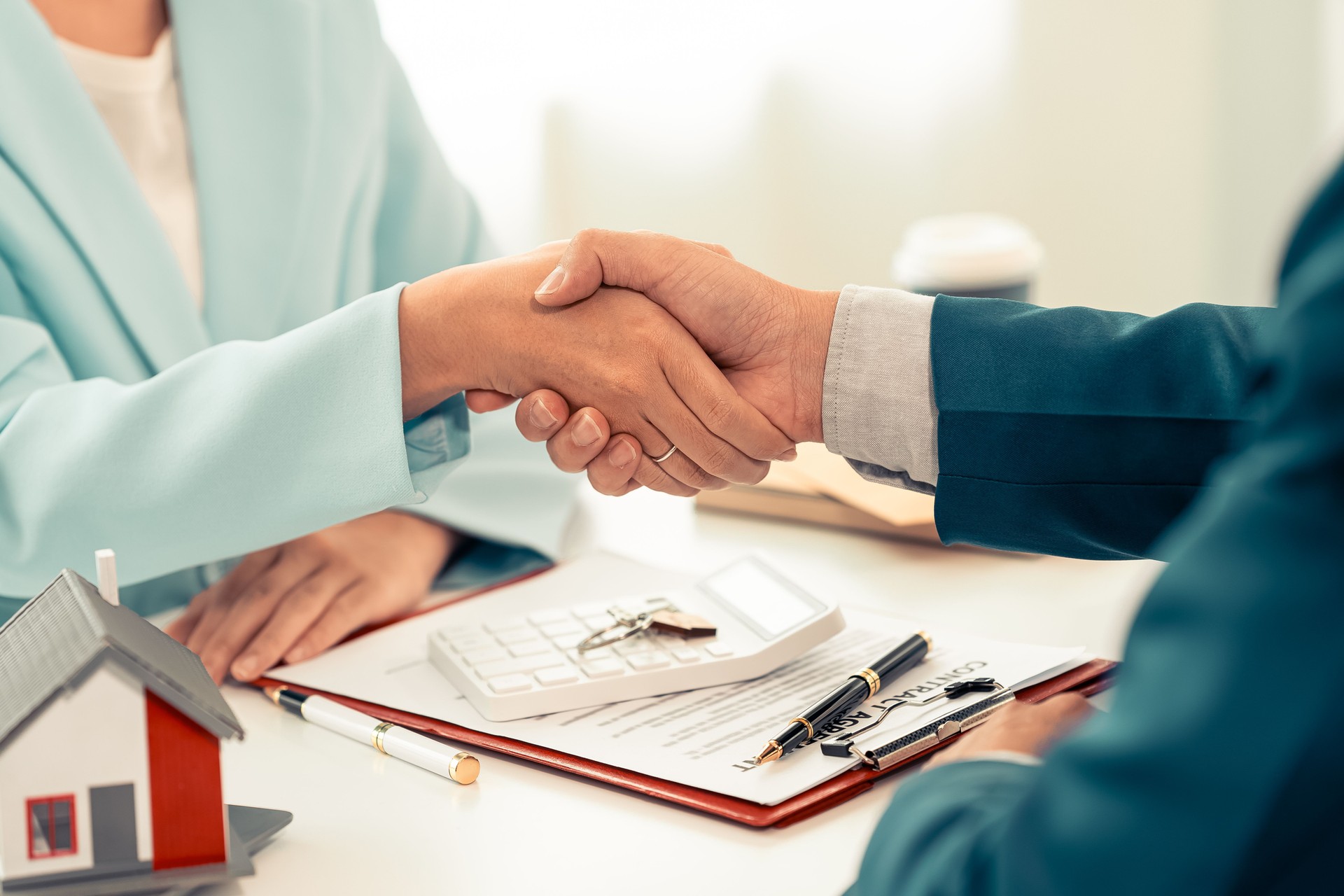 Home sales representative shakes hands with the client and negotiates successfully, and buying and selling handshakes sign the contract and successfully complete the purchase of the home.